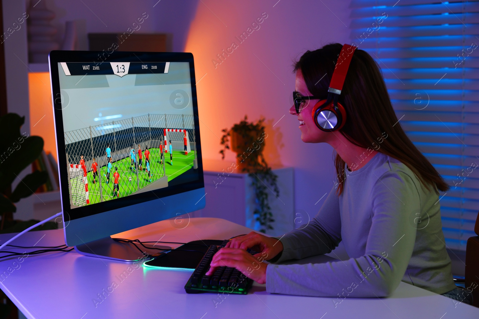 Photo of Smiling woman in headphones playing video game with keyboard at table indoors