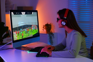 Photo of Smiling woman in headphones playing video game with keyboard at table indoors