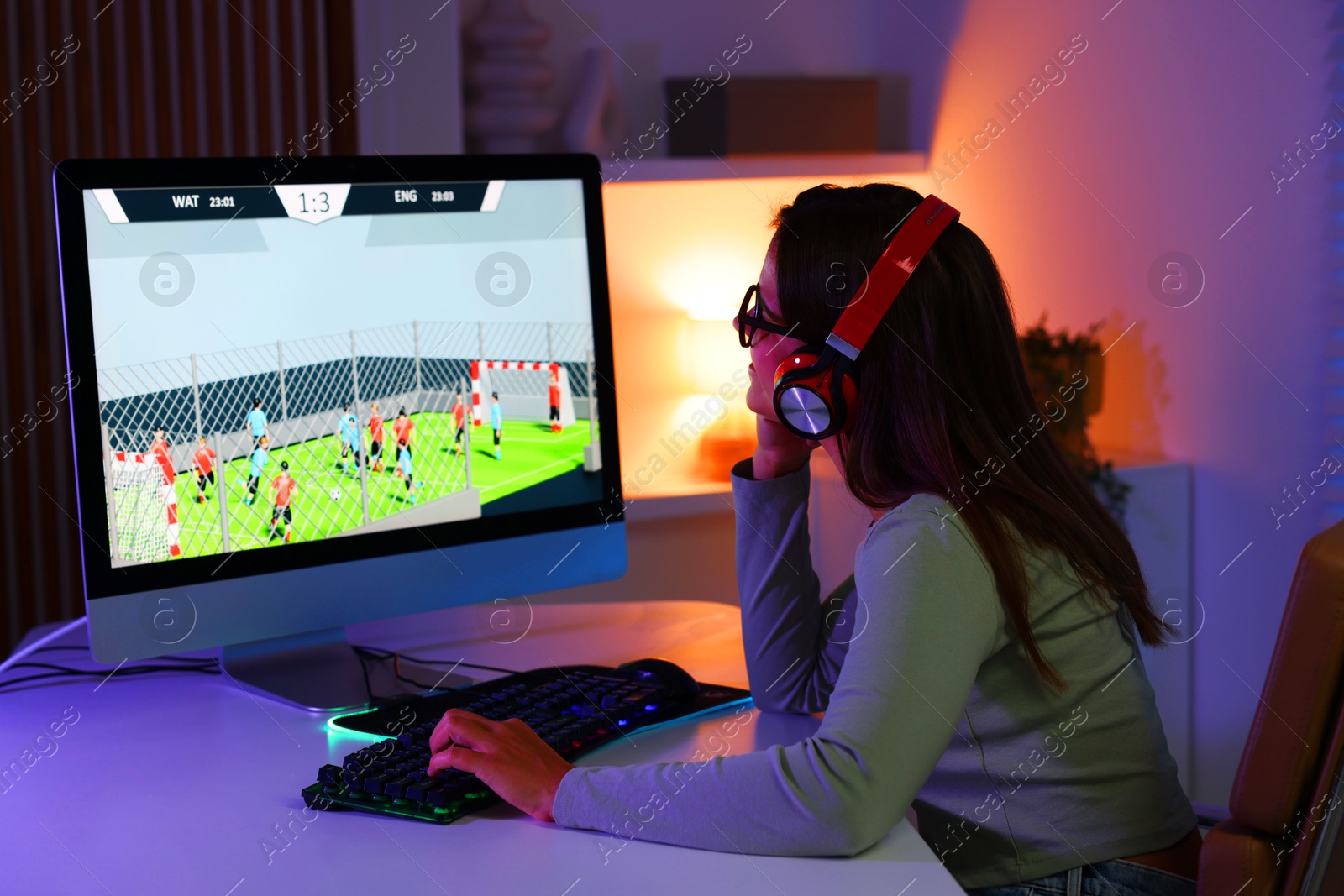 Photo of Woman in headphones playing video game with keyboard at table indoors