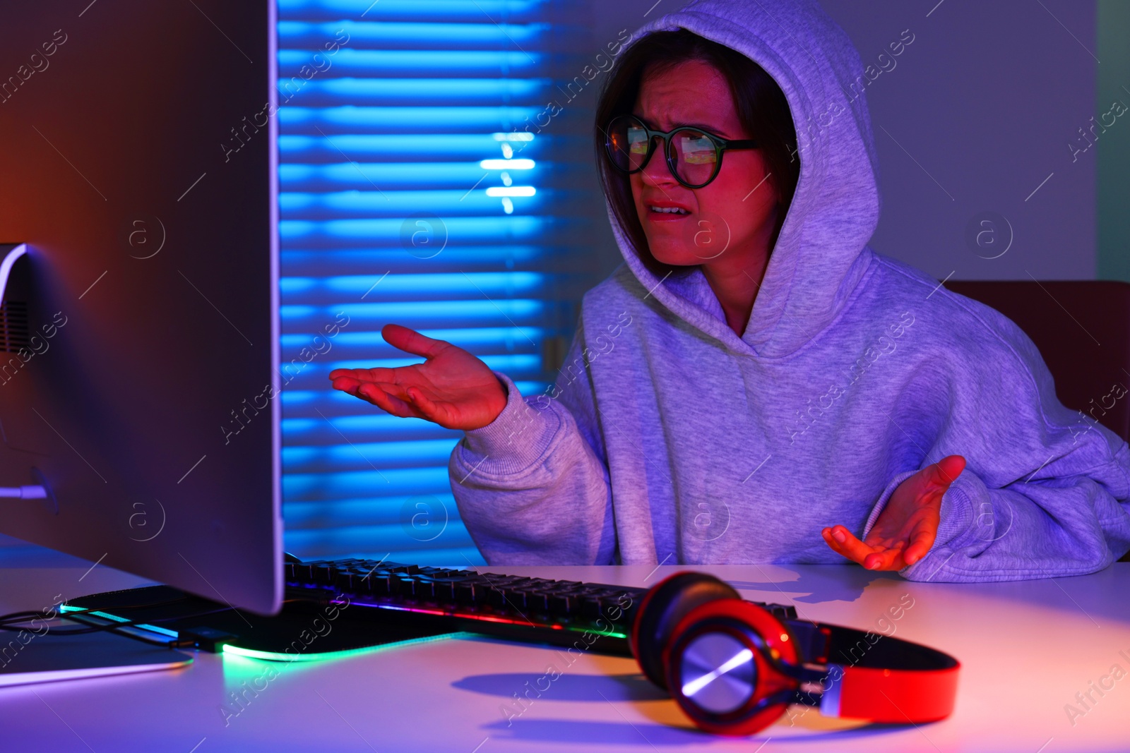 Photo of Emotional woman playing video game at table with keyboard, headphones and monitor indoors