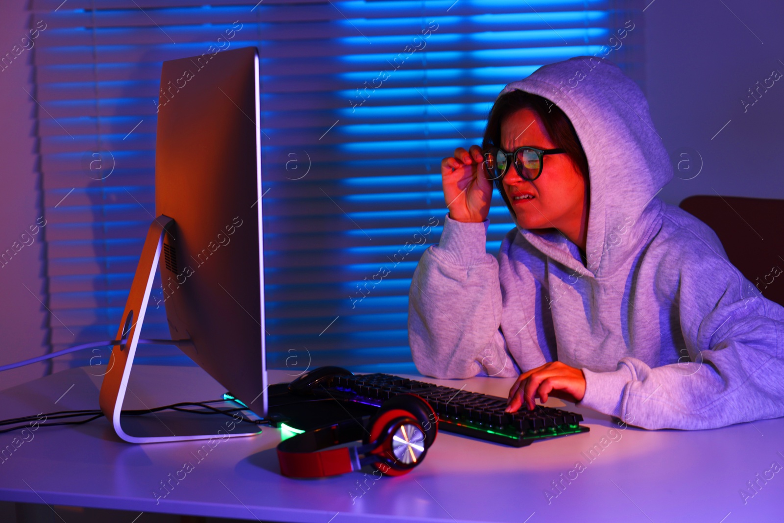 Photo of Emotional woman playing video game at table with keyboard, headphones and monitor indoors