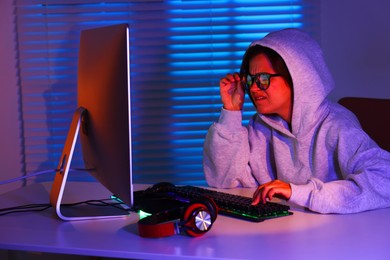 Photo of Emotional woman playing video game at table with keyboard, headphones and monitor indoors