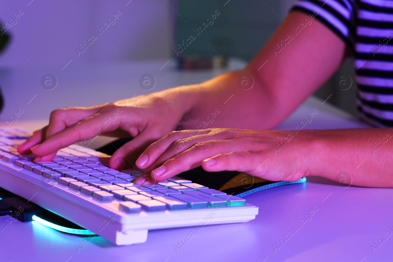 Photo of Woman using computer keyboard at white table indoors, closeup