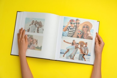 Photo of Woman looking at family photos in photo album on yellow background, top view