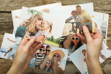 Photo of Woman with different photos in open photo album at wooden table, top view