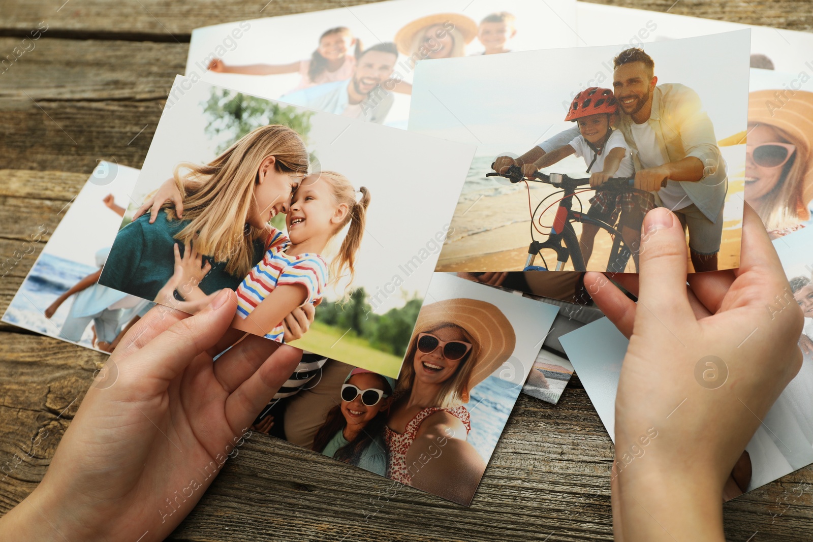 Photo of Woman with different photos in open photo album at wooden table, closeup