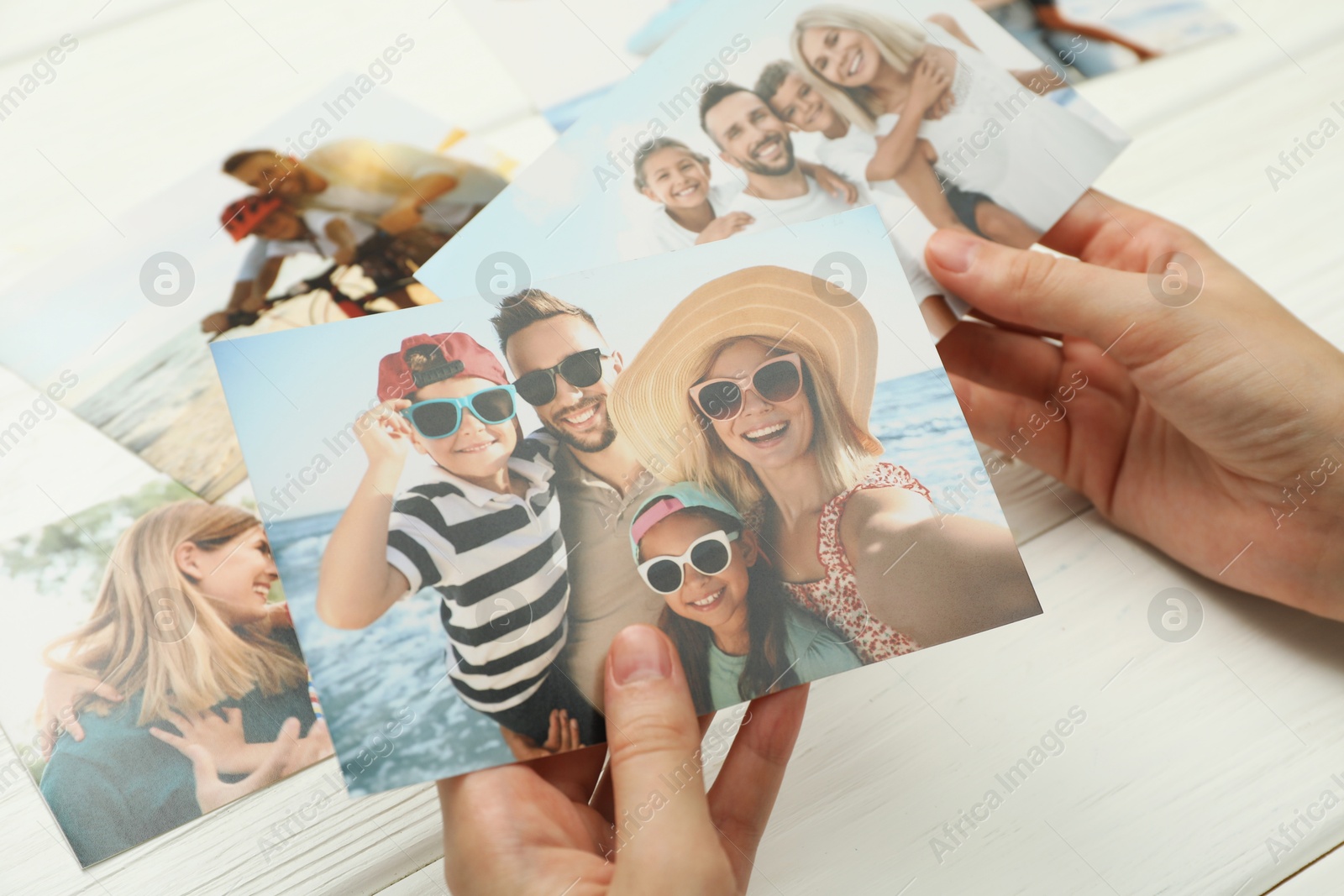 Photo of Woman with different photos at white wooden table, closeup