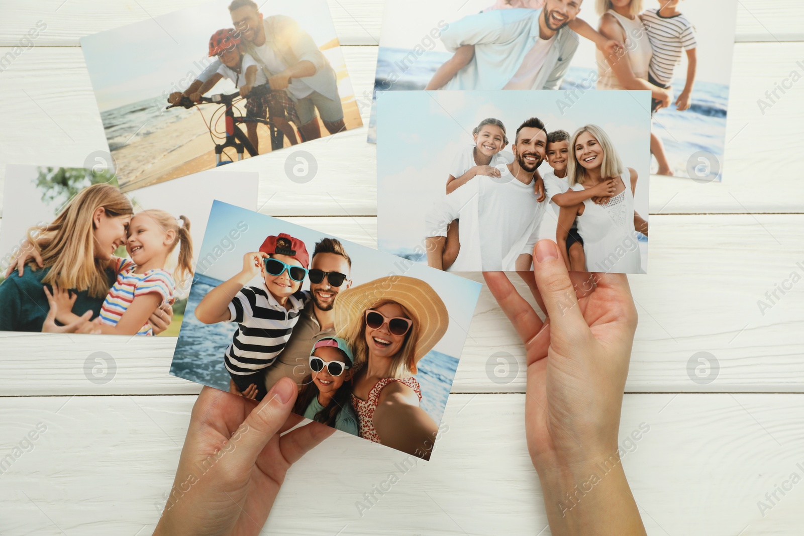 Photo of Woman with different photos at white wooden table, top view