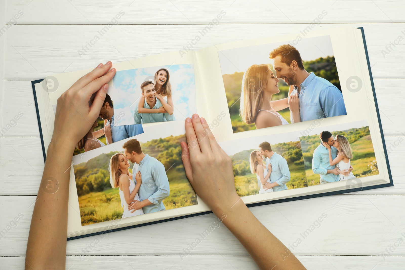 Photo of Woman with different photos in open photo album at white wooden table, top view