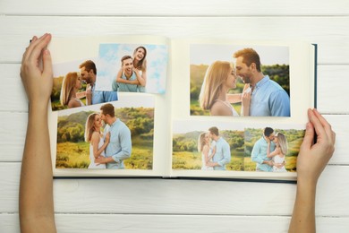 Photo of Woman with different photos in open photo album at white wooden table, top view