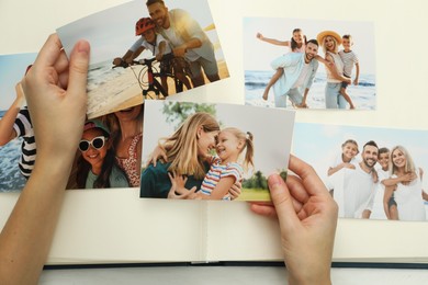 Photo of Woman with different photos in open photo album at white wooden table, top view