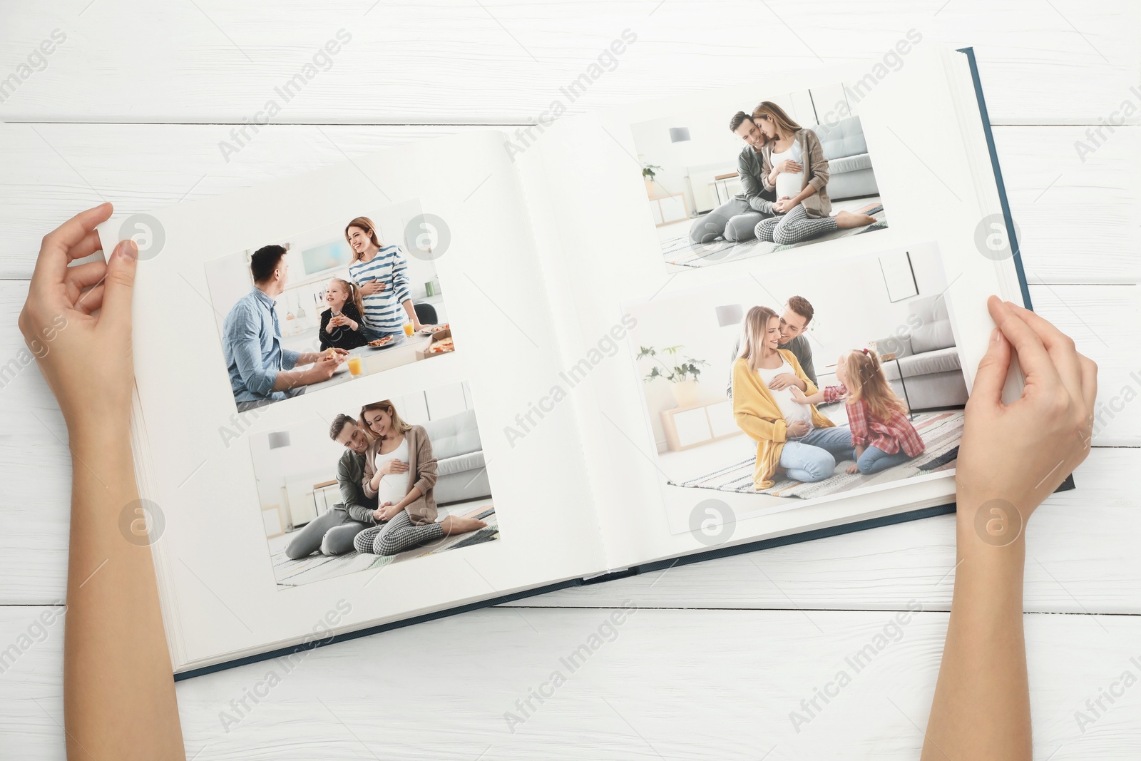 Photo of Woman with different photos in open photo album at white wooden table, top view