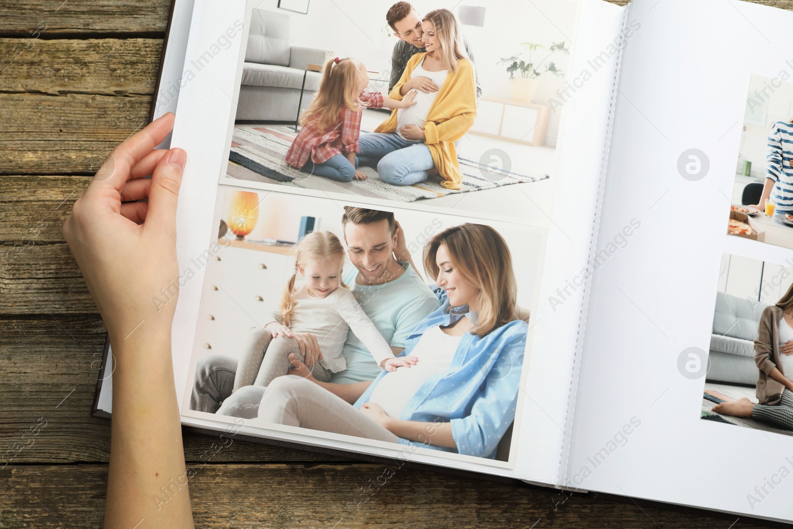 Photo of Woman with different photos in open photo album at wooden table, top view