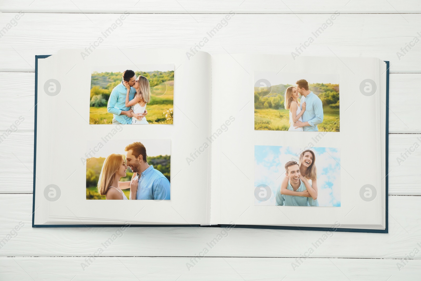 Photo of Different photos in open photo album on white wooden table, top view