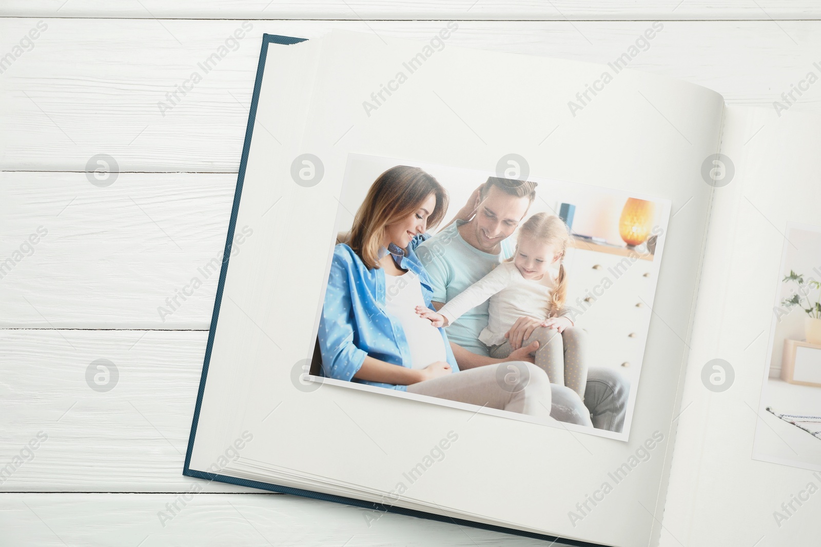 Photo of Different photos in open photo album on white wooden table, top view