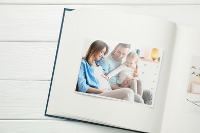 Photo of Different photos in open photo album on white wooden table, top view