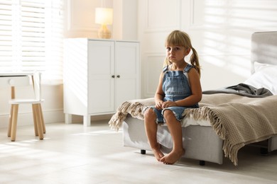 Photo of Orphanage concept. Sad little girl sitting on bed in child`s room