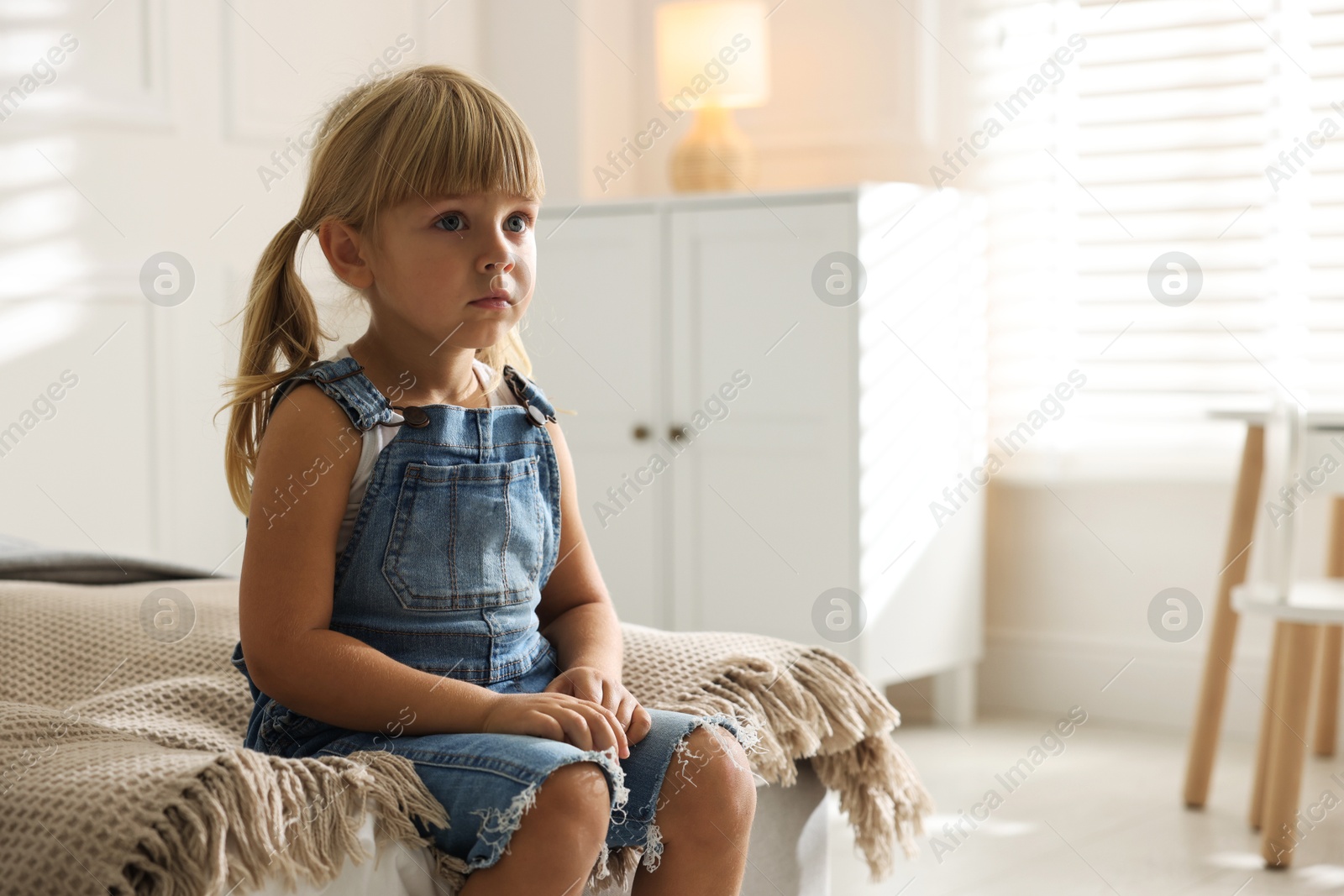 Photo of Orphanage concept. Sad little girl sitting on bed indoors, space for text