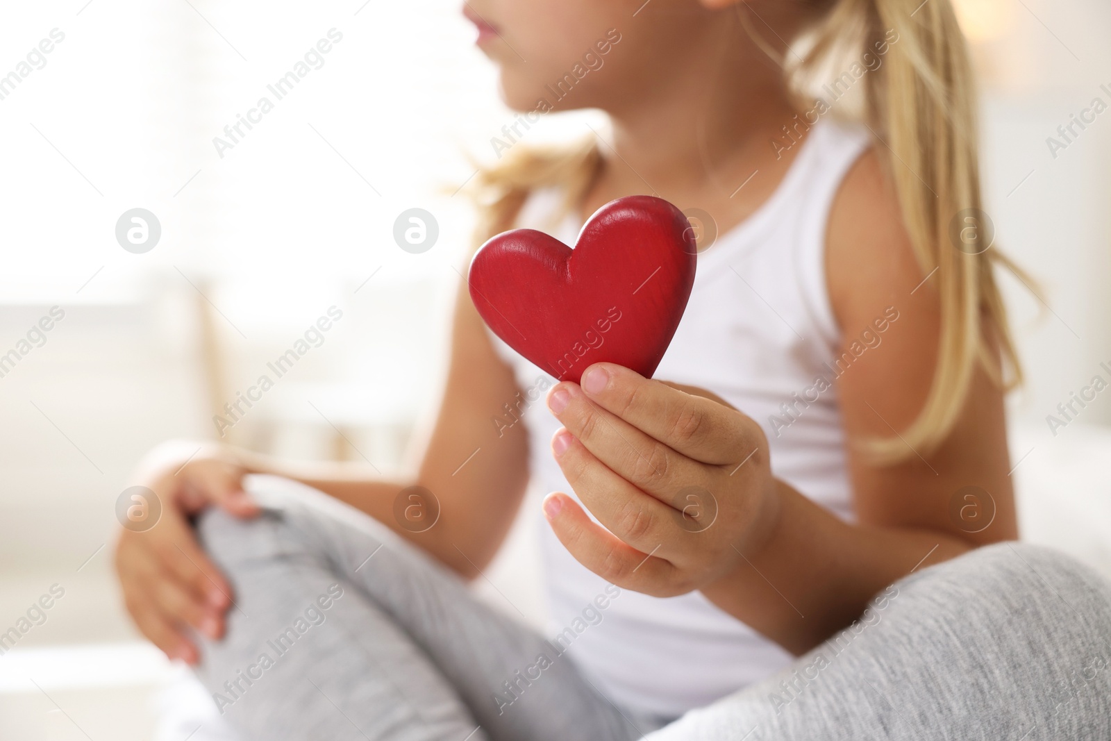 Photo of Orphanage concept. Little girl with red heart figure indoors, closeup