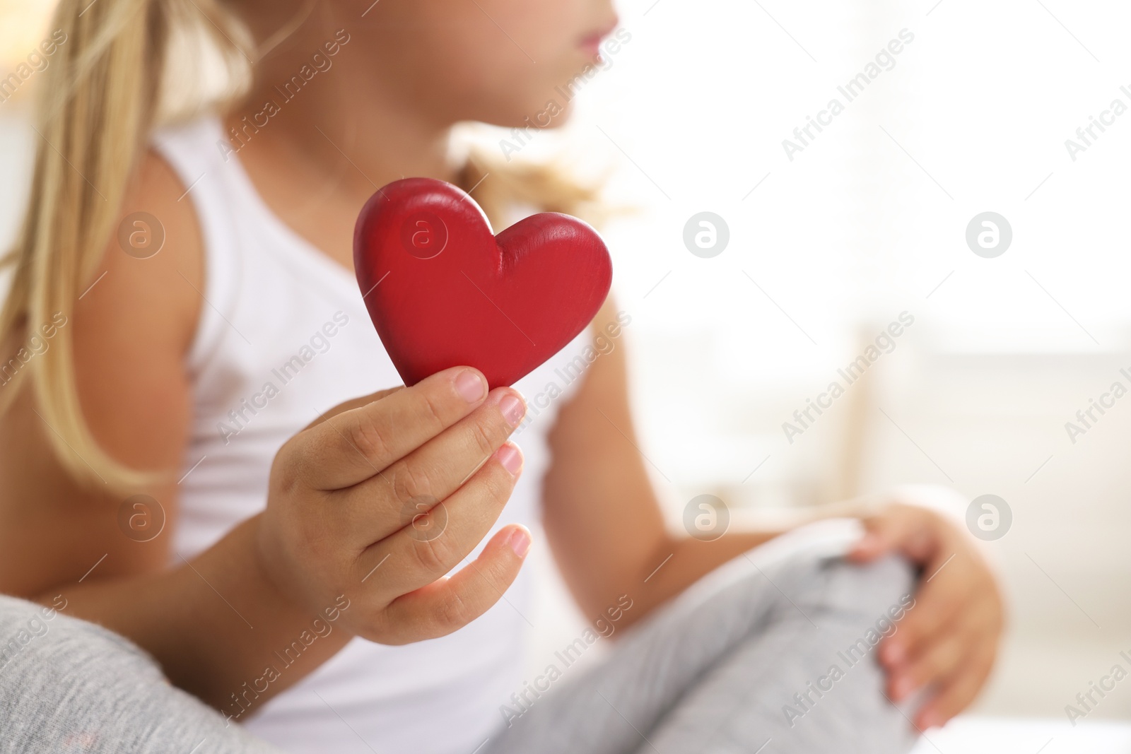 Photo of Orphanage concept. Little girl with red heart figure indoors, closeup. Space for text