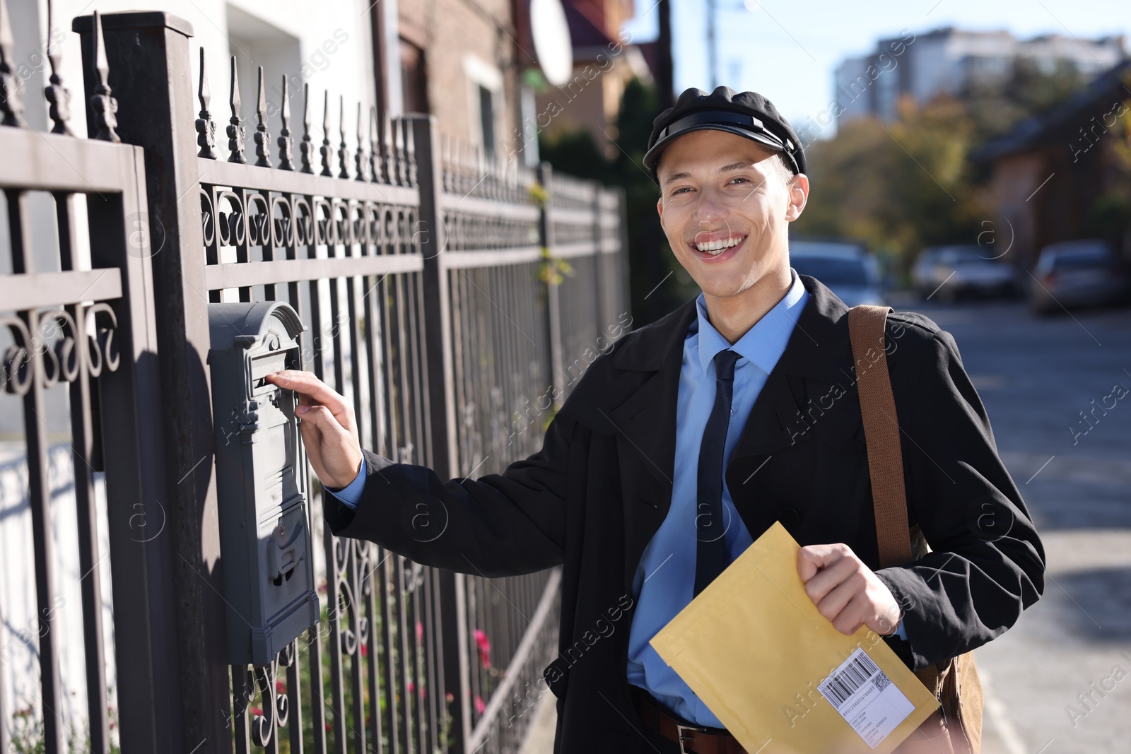 Photo of Happy postman putting envelope into mail box outdoors