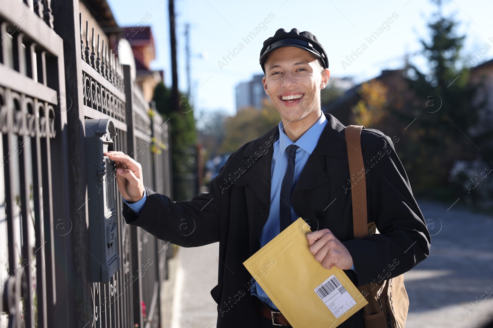 Photo of Happy postman putting envelope into mail box outdoors