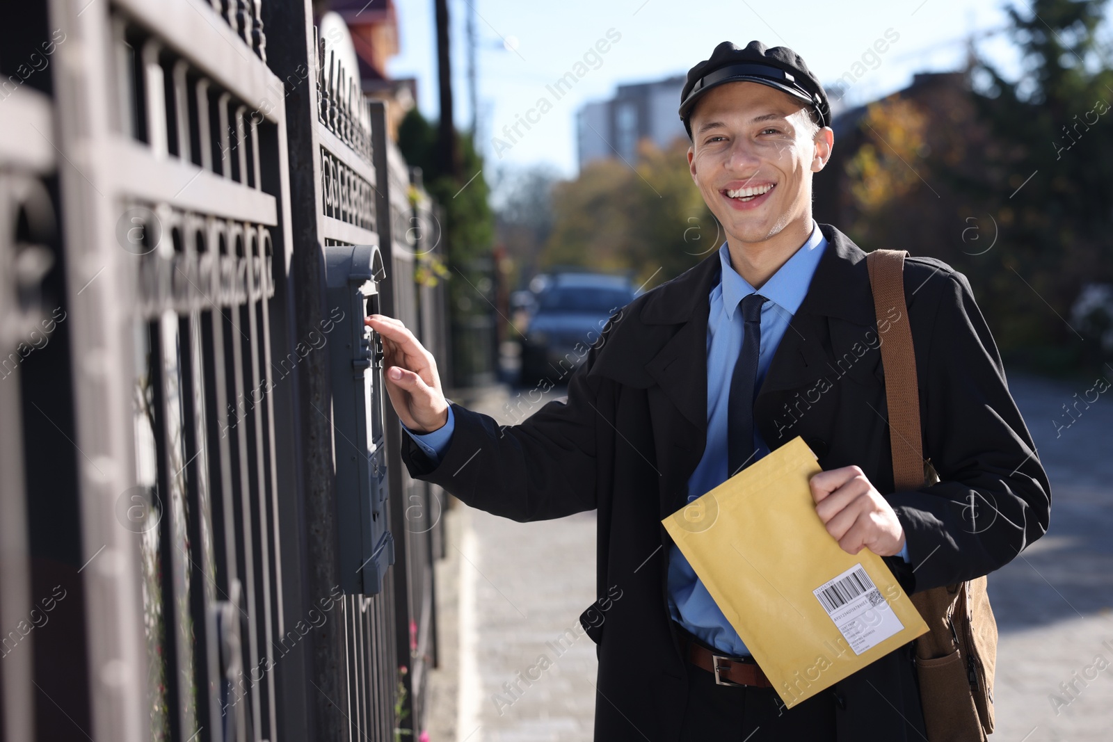 Photo of Happy postman putting envelope into mail box outdoors