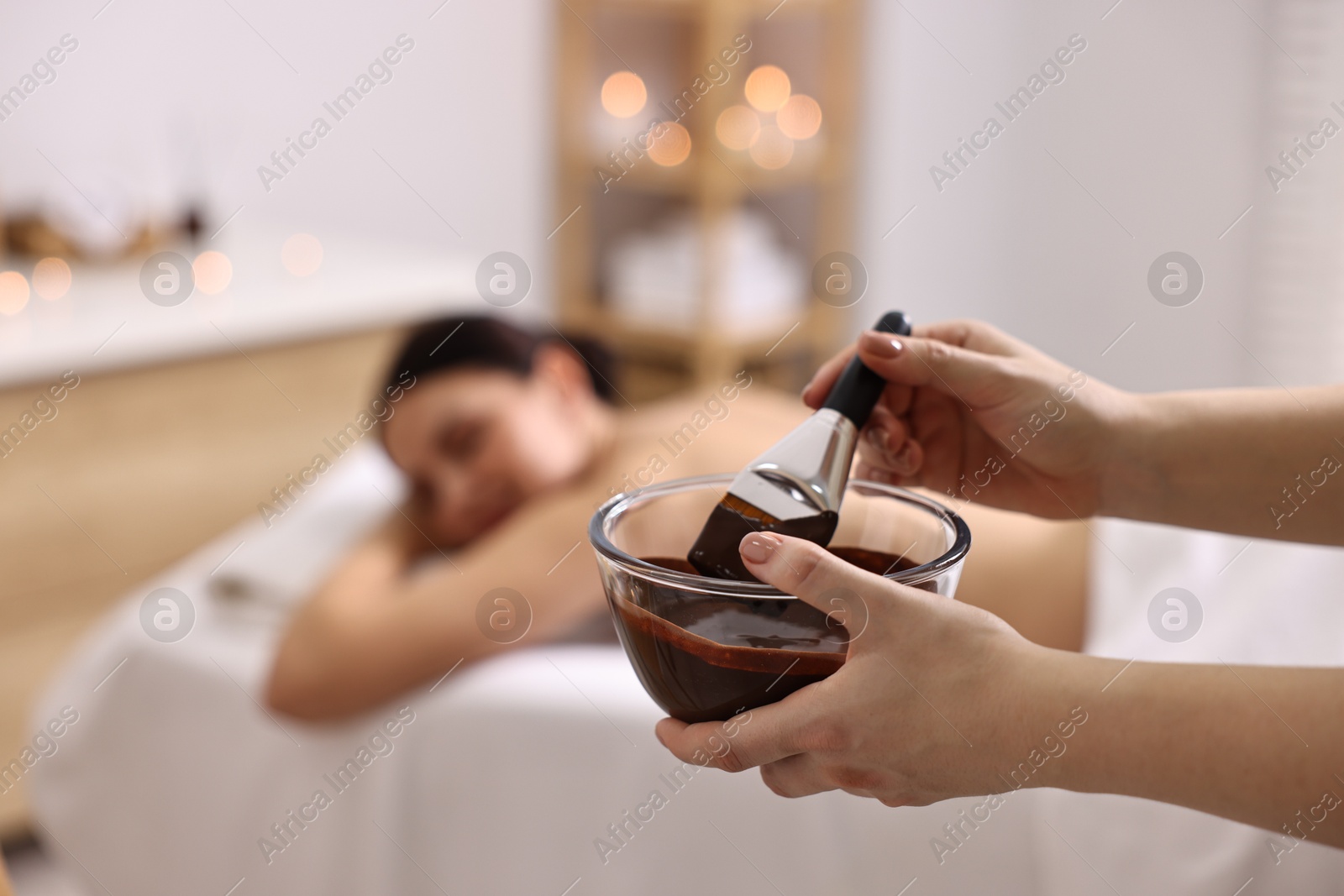 Photo of Spa worker with cosmetic product for chocolate body wrap near woman in salon, closeup. Selective focus