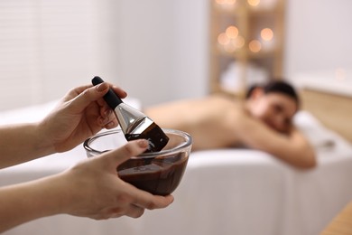 Photo of Spa worker with cosmetic product for chocolate body wrap near woman in salon, closeup. Selective focus