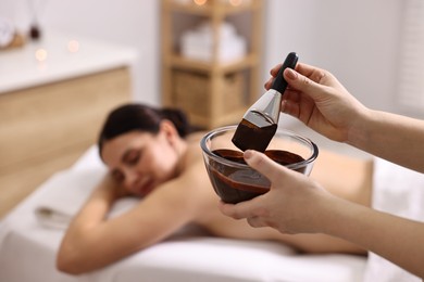 Photo of Spa worker with cosmetic product for chocolate body wrap near woman in salon, closeup. Selective focus