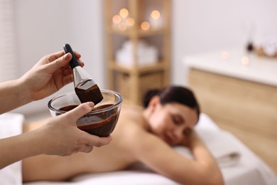 Photo of Spa worker with cosmetic product for chocolate body wrap near woman in salon, closeup. Selective focus