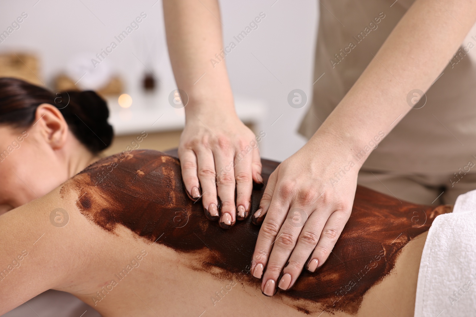 Photo of Woman undergoing chocolate body wrap treatment in spa salon, closeup