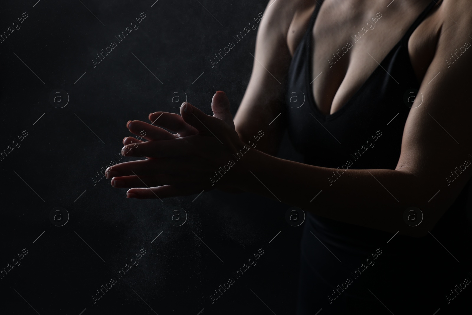 Photo of Woman clapping hands with talcum powder before training on black background, closeup