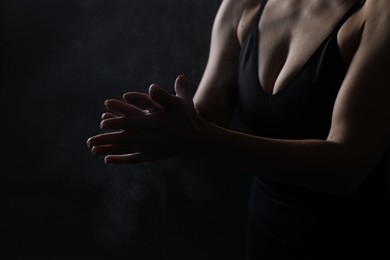 Photo of Woman clapping hands with talcum powder before training on black background, closeup