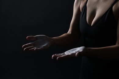 Photo of Woman with talcum powder on her hands before training against black background, closeup