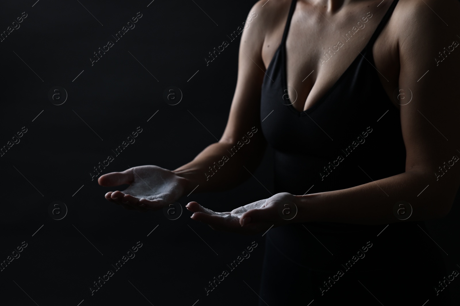 Photo of Woman with talcum powder on her hands before training against black background, closeup