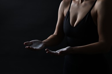 Photo of Woman with talcum powder on her hands before training against black background, closeup