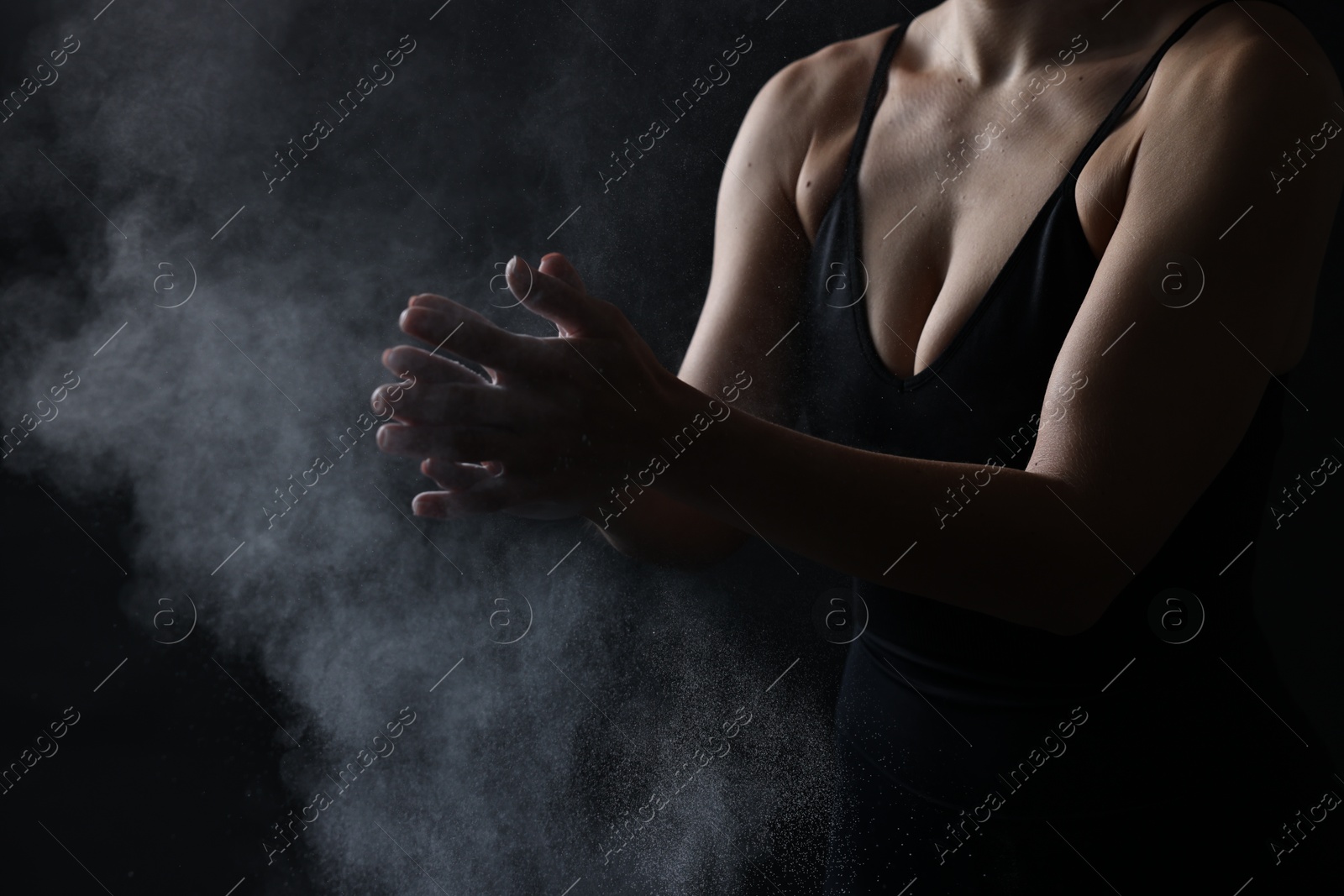 Photo of Woman clapping hands with talcum powder before training on black background, closeup