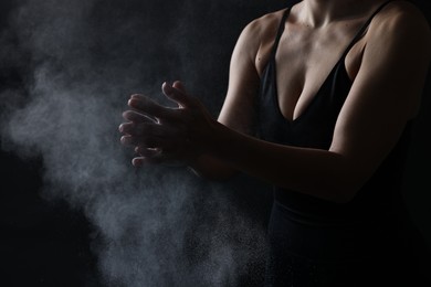 Photo of Woman clapping hands with talcum powder before training on black background, closeup