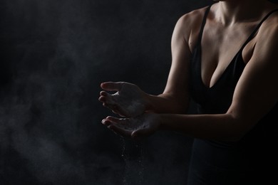 Photo of Woman with talcum powder on her hands before training against black background, closeup. Space for text