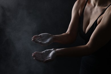 Photo of Woman with talcum powder on her hands before training against black background, closeup. Space for text