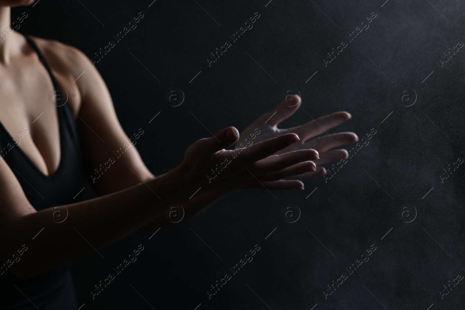 Photo of Woman clapping hands with talcum powder before training on black background, closeup