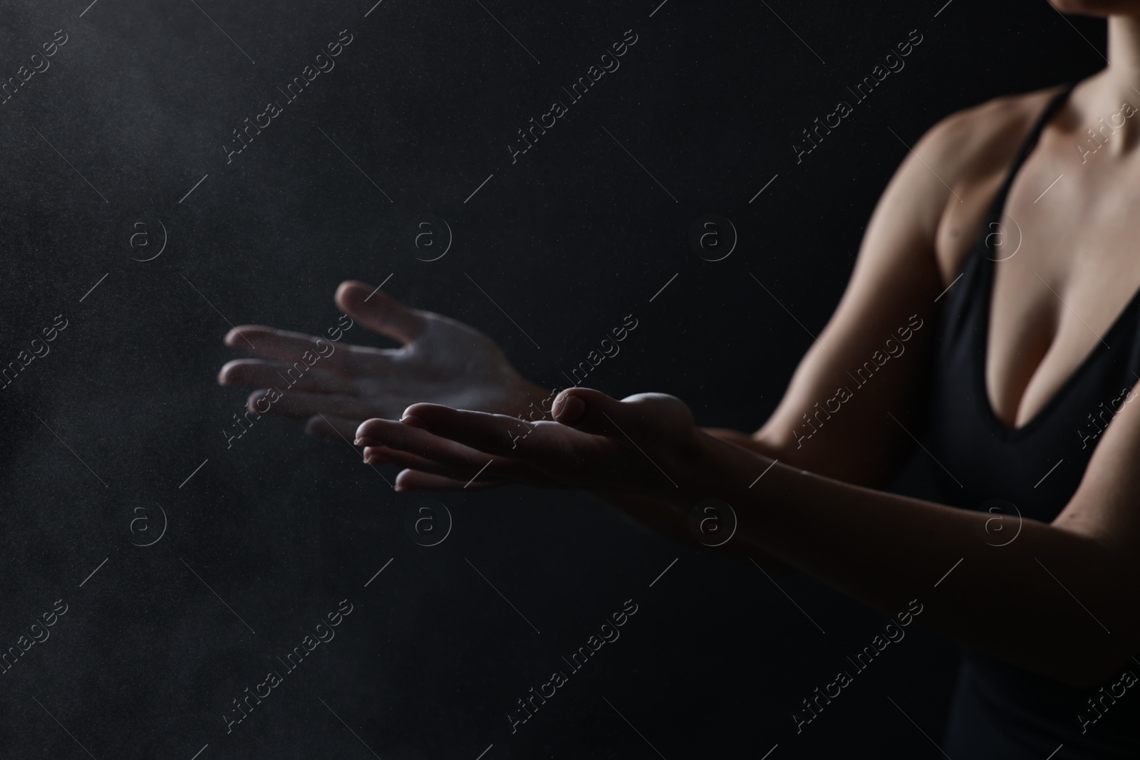 Photo of Woman clapping hands with talcum powder before training on black background, closeup