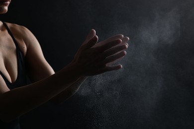 Photo of Woman clapping hands with talcum powder before training on black background, closeup. Space for text