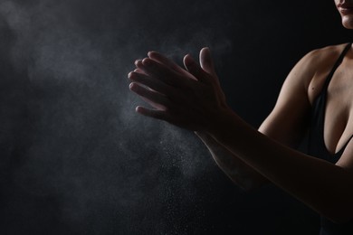 Photo of Woman clapping hands with talcum powder before training on black background, closeup. Space for text