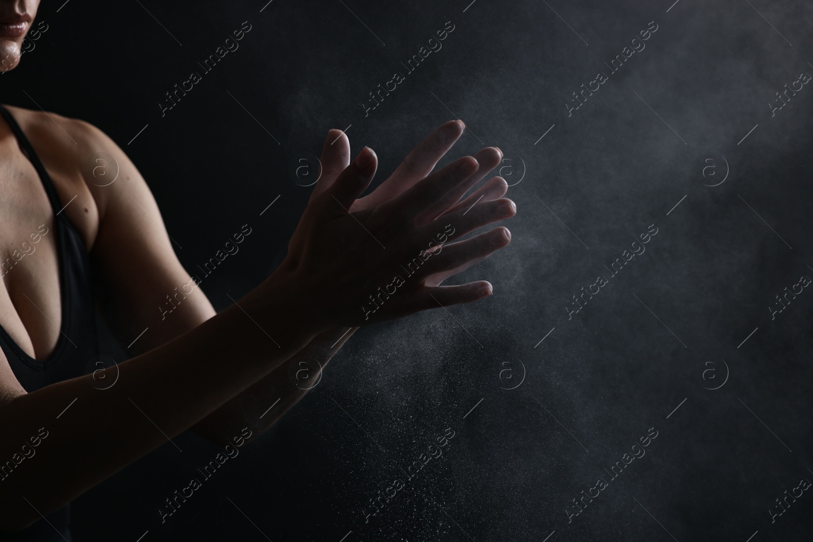 Photo of Woman clapping hands with talcum powder before training on black background, closeup. Space for text