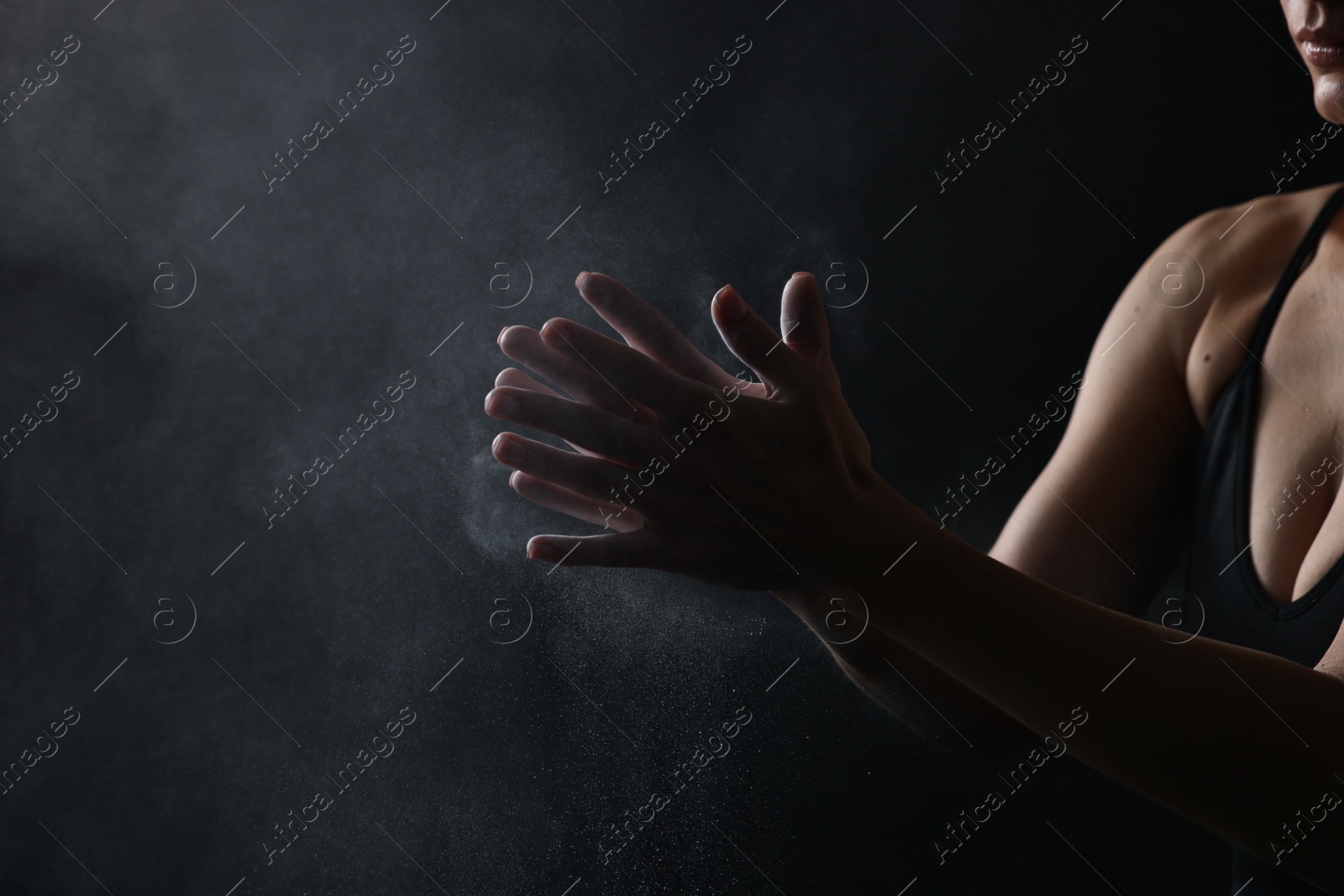 Photo of Woman clapping hands with talcum powder before training on black background, closeup. Space for text