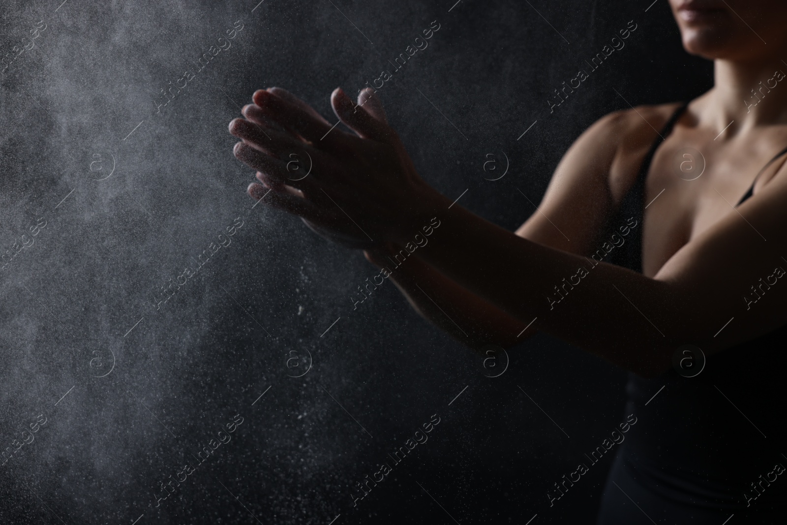 Photo of Woman clapping hands with talcum powder before training on black background, closeup. Space for text