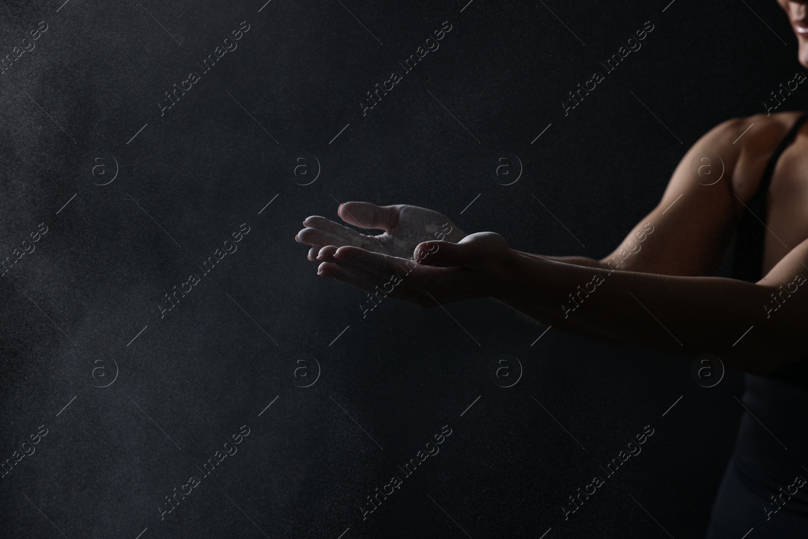 Photo of Woman with talcum powder on her hands before training against black background, closeup. Space for text