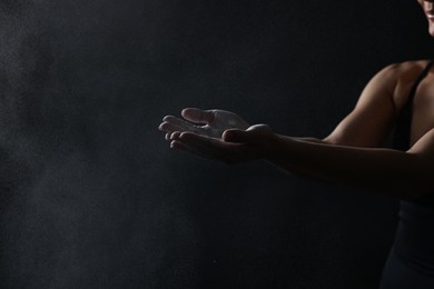 Photo of Woman with talcum powder on her hands before training against black background, closeup. Space for text